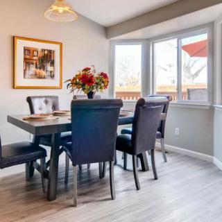 A modern dining room with a table and chairs set, adorned with a floral centerpiece near large windows.