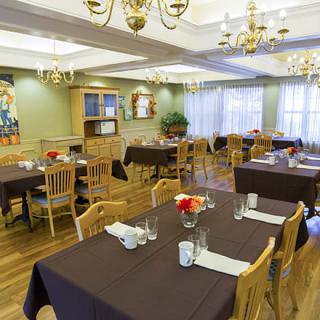 An elegant dining room with tables set for service, featuring chandeliers and wooden decor.