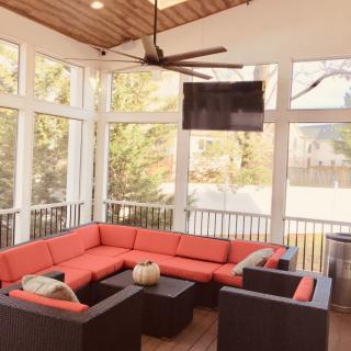 A cozy sunroom with a large red sectional sofa, ceiling fan, and mounted TV.