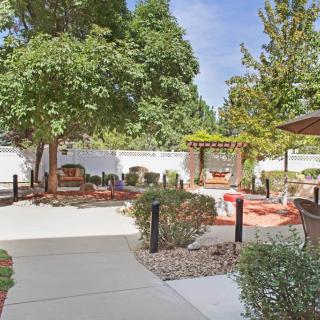 A tranquil garden setting with a paved pathway, seating area, lush trees, and a pergola.