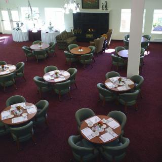 Empty dining area with round tables and chairs on a carpeted floor.