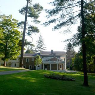A large mansion surrounded by tall trees and a well-maintained lawn.