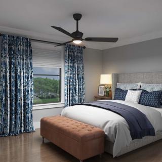 A cozy and elegantly furnished bedroom featuring a ceiling fan, large window with blue patterned curtains, a well-made bed with blue accents, and a bedside lamp.