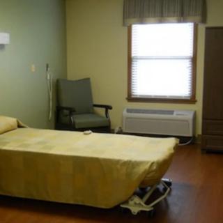 A minimalist hospital room with a single bed, chair, and window.