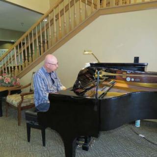 A person playing a grand piano indoors near a staircase.