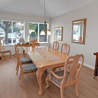 A bright dining room featuring a wooden table with matching chairs, pendant lighting, and large windows offering natural light.