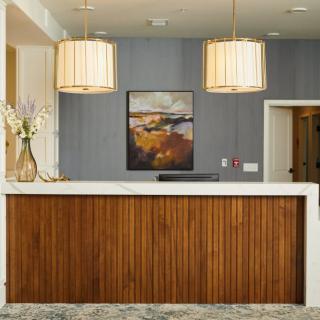 A modern hotel reception area featuring a wooden desk, pendant lights, and stylish artwork.