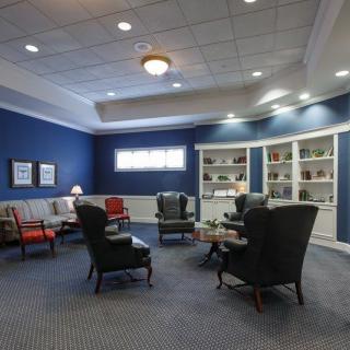 A cozy living room with a seating area featuring various chairs, sofas, and bookshelves against blue walls.