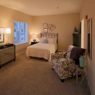 A cozy bedroom with warm lighting, featuring a bed, armchair, and stylish decor.