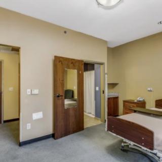 An empty hospital room with a bed and wooden furniture.