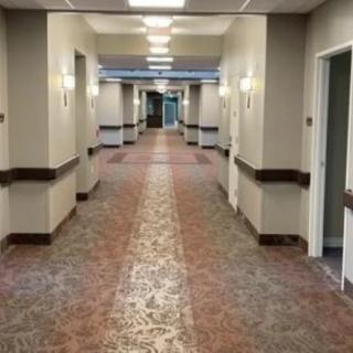 A well-lit hospital hallway with multiple doors and a patterned carpet.