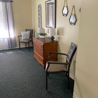 A cozy room corner with a wooden dresser, two chairs, and decorative mirrors on the wall.