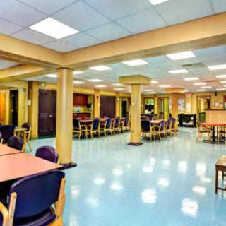 An empty dining hall with neatly arranged tables and chairs, illuminated by ceiling lights.