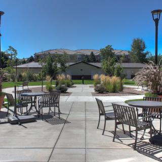 A peaceful outdoor patio area with tables and chairs, surrounded by a landscaped garden and trees.