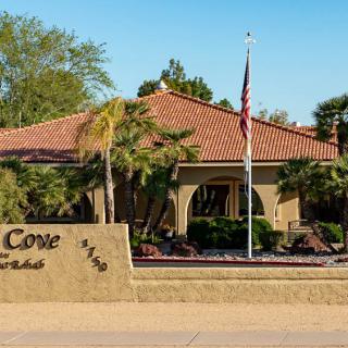 A building entrance with a sign and flag, surrounded by landscaping and palm trees.