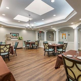 A well-lit dining area with elegantly arranged tables and chairs, featuring wood flooring and decorative elements.