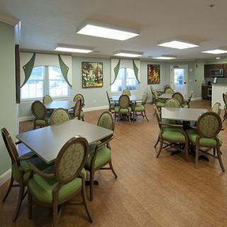An elegant dining area with green chairs and square tables, featuring large windows with drapes.