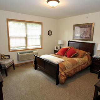 A cozy bedroom with a neatly made bed, wooden furniture, and natural light from the window.