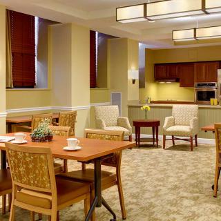 A modern dining area with wooden tables and chairs, adjacent to a kitchen.