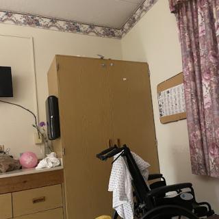 A patient room featuring a wheelchair, a television mounted on the wall, and a storage cabinet.