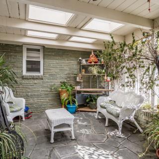 A cozy sunroom featuring white wicker furniture, abundant indoor plants, and ample natural light streaming in through skylights.