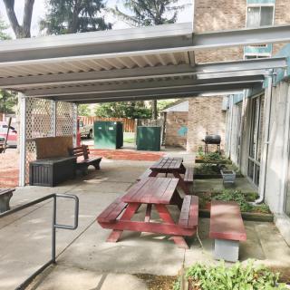 Covered outdoor seating area with picnic tables and benches in an urban environment.