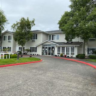 A two-story residential building with a driveway and trees under a cloudy sky.