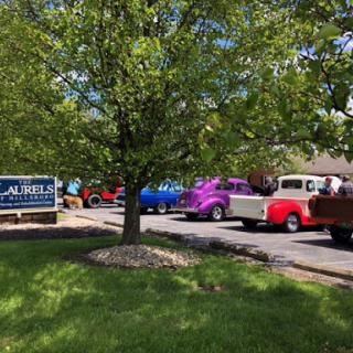 A lineup of vibrant vintage trucks parked near a sign, surrounded by lush greenery.
