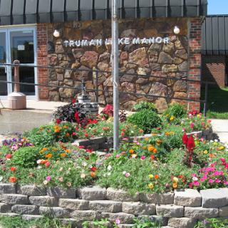 A vibrant garden blooms in front of a stone-faced building, complete with a flagpole.
