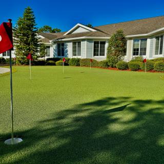 A putting green in front of a residential building on a sunny day.