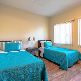 A bright bedroom with two single beds featuring turquoise bedding and a wooden floor.