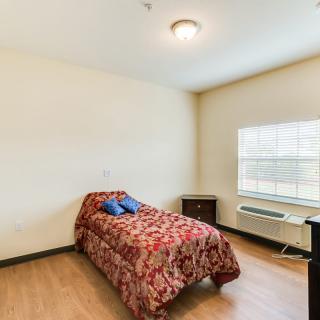 A simple bedroom featuring a single bed with a floral cover, a bedside table, and a window letting in natural light.