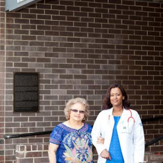A doctor poses with a patient outside a healthcare facility.