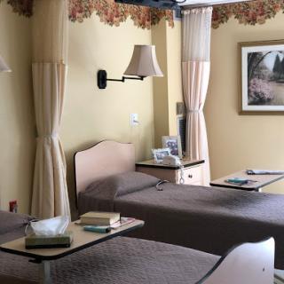 A serene hospital patient room featuring two beds, elegant curtains, and a calming piece of artwork.