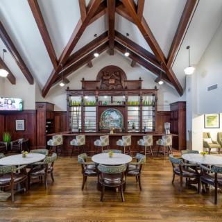 A spacious restaurant interior featuring high ceilings with wooden beams, a bar area, and multiple tables and chairs.