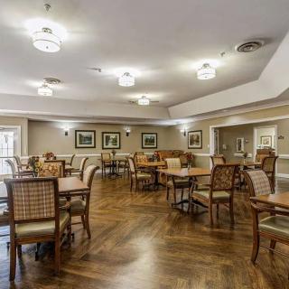 A spacious dining room with arranged tables and chairs, featuring elegant lighting and hardwood flooring.