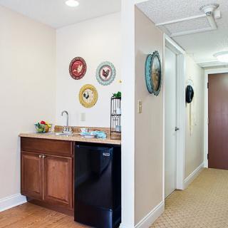 A small kitchenette area with wall-mounted decorative plates and a mini fridge next to a hallway.