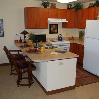 A cozy kitchen with wooden cabinets, a refrigerator, and a counter with stools.