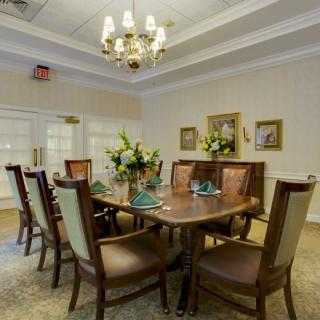 A traditional dining room featuring a wooden table, elegant chairs, and a chandelier overhead. The room is decorated with flowers and paintings on the walls.