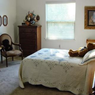 A cozy, well-lit bedroom with a bed, dresser, and chair.