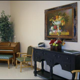 A cozy room interior featuring a small piano, elegant furniture, and a vibrant still-life painting on the wall.
