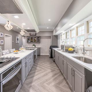 A modern kitchen with gray cabinets, ample countertops, and large windows providing bright natural light.