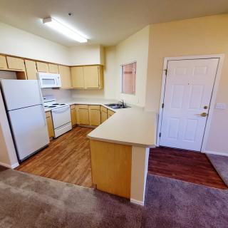 A cozy apartment kitchen with wood flooring, featuring a fridge, oven, microwave, and ample countertop space.