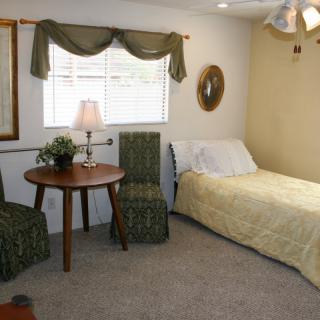A cozy bedroom with a single bed, a small round table, and two chairs near a window with curtains.