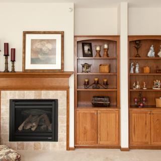 A cozy living room with a fireplace and wooden bookshelves adorned with decorative items.