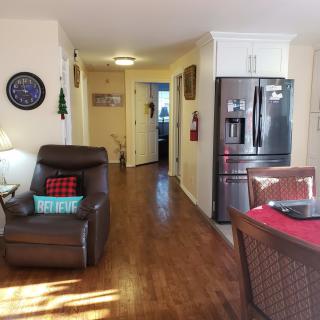 A cozy living space with a leather armchair, hardwood flooring, and an adjacent kitchen with a modern refrigerator.