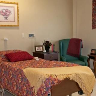A cozy hospital room featuring a single bed with patterned bedding, an armchair, and decorative elements.