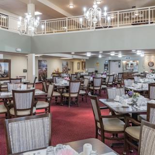 An elegant dining area featuring multiple tables and chairs, complete with chandeliers and a carpeted floor.