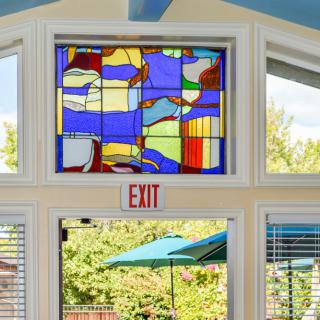Stained glass window with abstract design above an exit in a brightly lit room.