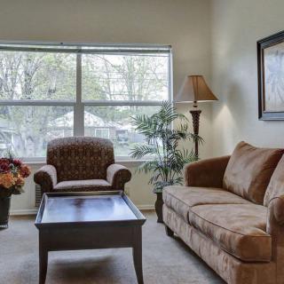 A cozy living room featuring a sofa, armchair, and a coffee table, illuminated by natural light from a large window.